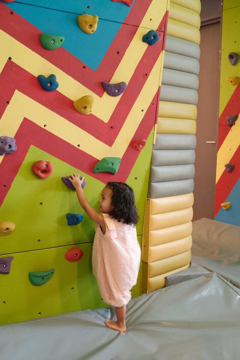 A young child climbs a colorful indoor climbing wall