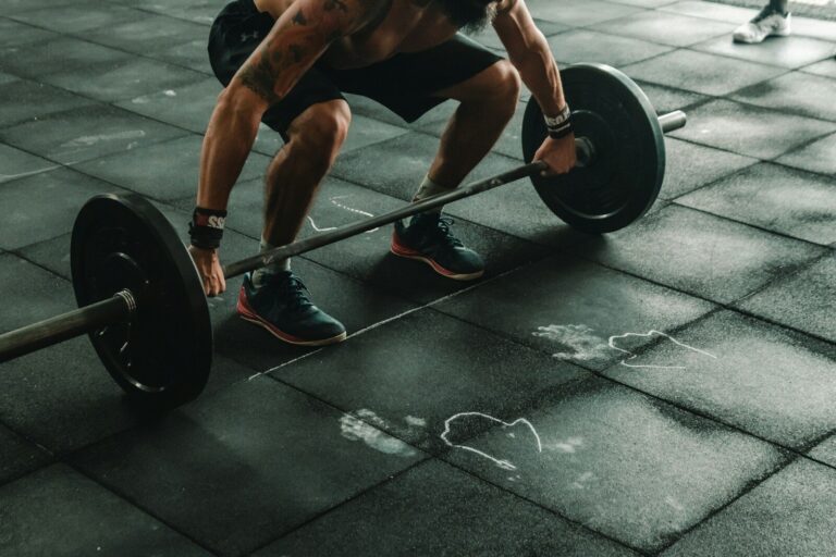A person lifting a heavy barbell from a black rubber gym floor